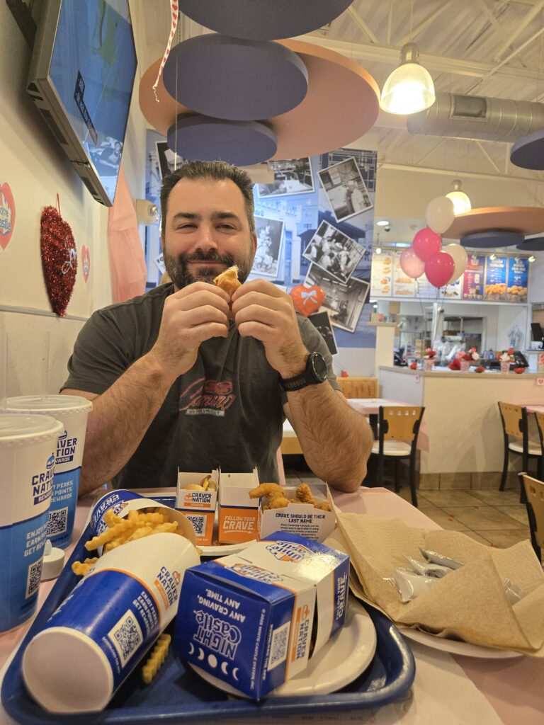 Interior of White Castle Restaurant. Patron smiles and eats his food. 