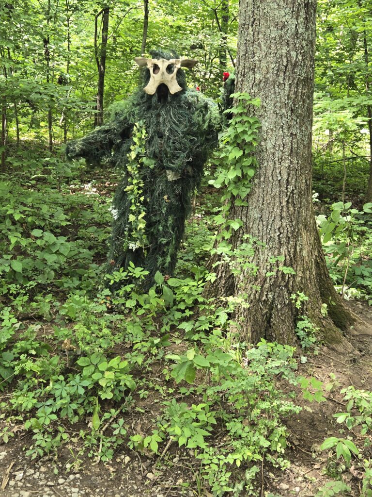 Man wearing green man costume with skull and green gilly suit